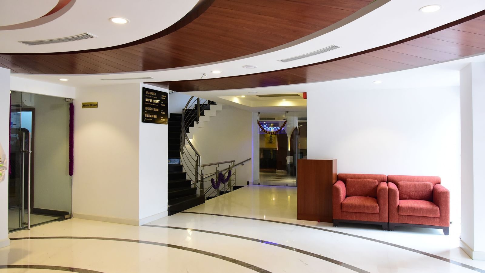 The contemporary and spacious lobby of The Royal Comfort, showcasing a curved ceiling design and a small seating area with red sofas.