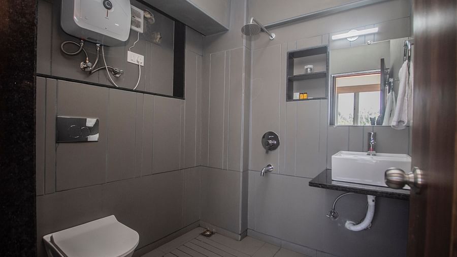 Modern bathroom with a wall-mounted toilet, overhead shower, sink with vanity mirror, water heater, and minimal grey-toned décor - Central Heritage Resort and Spa