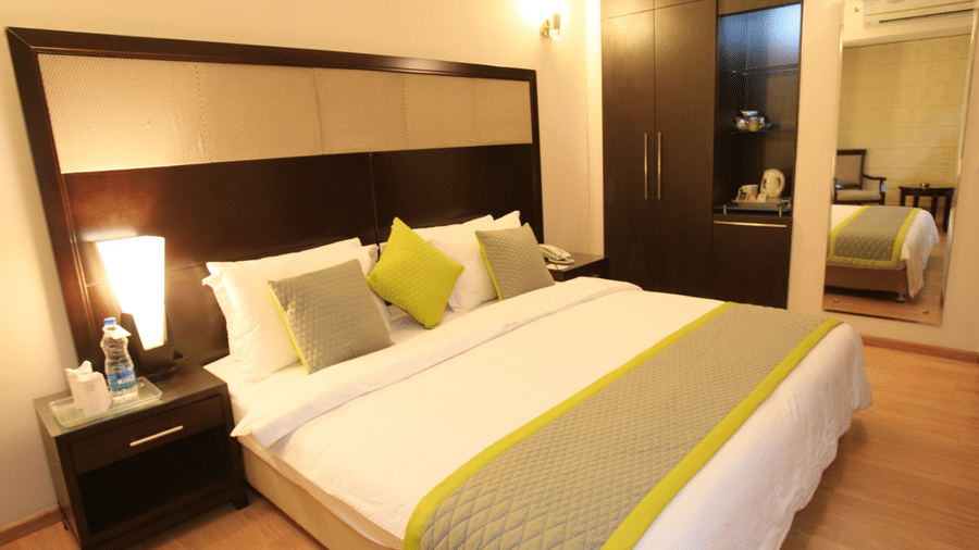 Executive room at Emblem Hotel, New Friends Colony, New Delhi featuring a double size bed, a bedside table, a wardrobe, a tea and coffee maker, and a mirror attached on the wall.