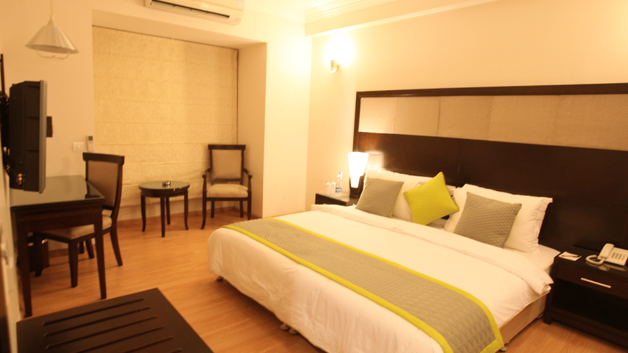 Executive room at Emblem Hotel, New Friends Colony, New Delhi featuring a double size bed, a work desk and chair, a chair with centre table, and a flat TV screen on the wall.