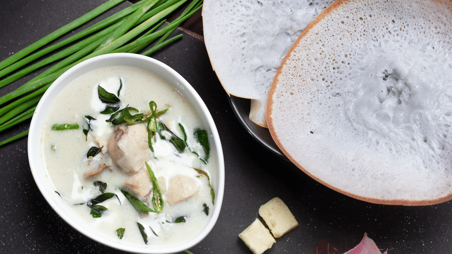Appam with vegetable stew served on a wooden surface with curry leaves and diced butter at Paradise Lagoon Resort, Udupi.