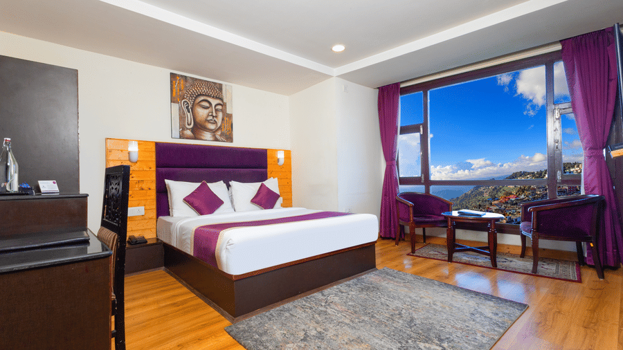 Comfortable living space at Sumitel Hotels with wooden ceilings, stone accent walls, plush bedding, flat-screen TV, seating area, and large windows bringing in natural light
