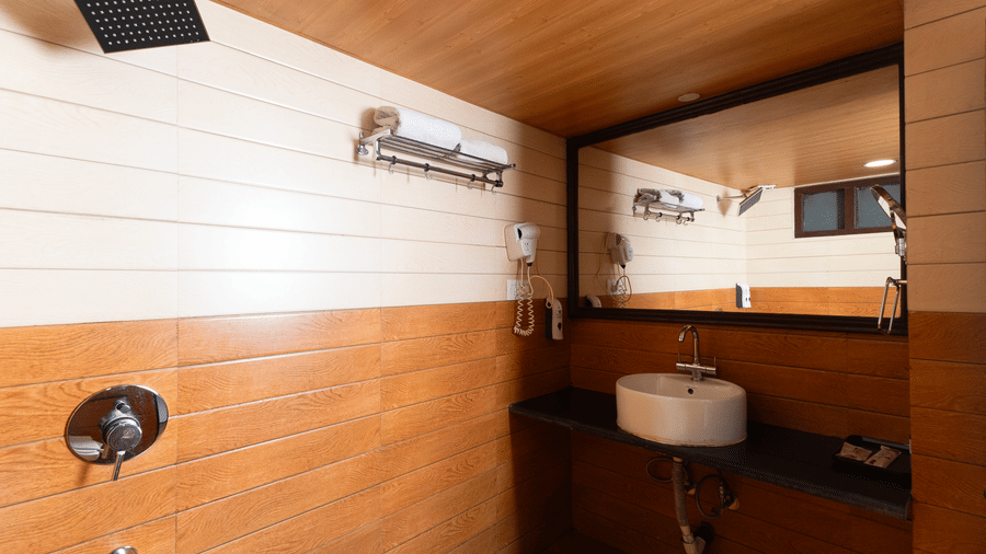 Stylish wash basin area at Sumitel Hotels featuring a modern round sink, large mirror, wooden and white panel walls, sleek countertop, and warm ambient lighting.