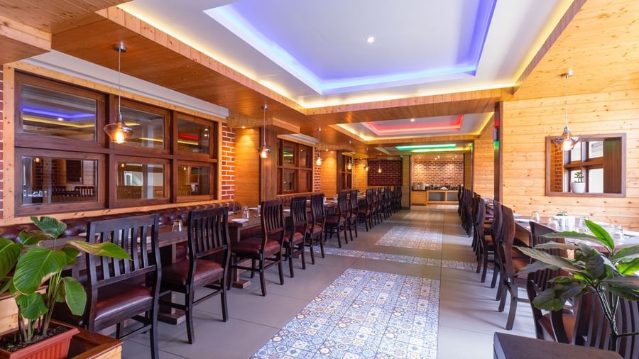 Restaurant at Sumitel Premier Inn, Siliguri, with warm lighting, wooden interiors, decorative plants, and neatly arranged seating offering guests a cosy dining space.