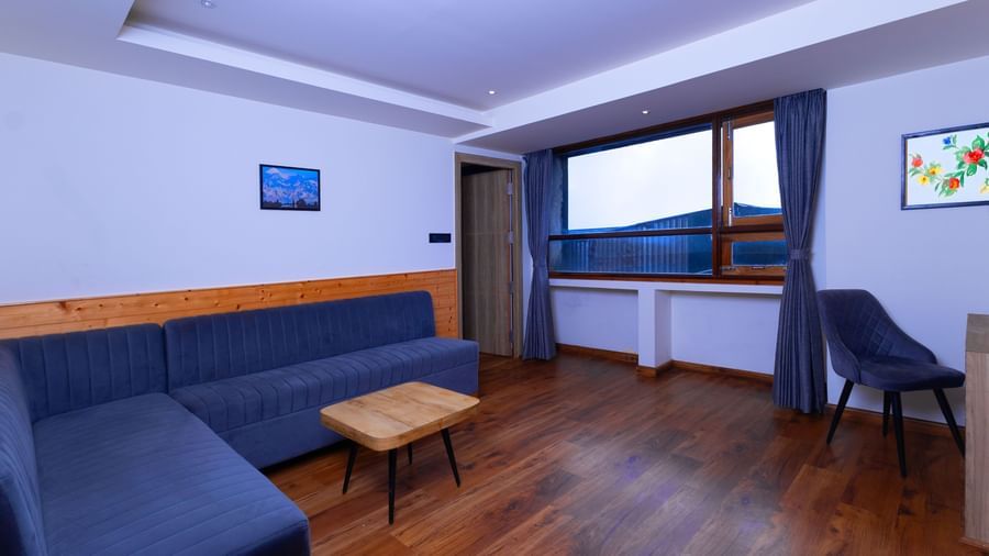 Guest room seating area at Sumitel Premier Inn, Siliguri, with a sofa set, wooden table, and large window offering a bright and comfortable space.