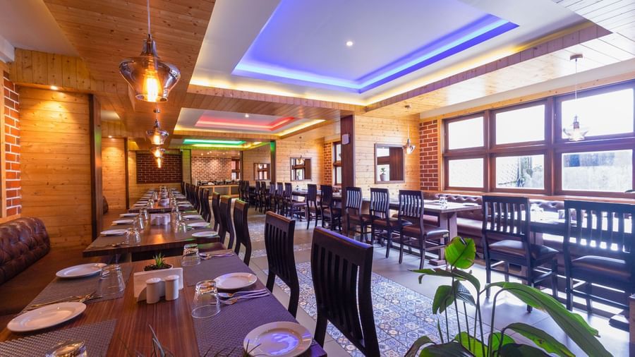 Modern restaurant at Sumitel Premier Inn, Siliguri, with colourful ceiling lights, wooden furniture, and neatly arranged dining tables for guests to enjoy meals.