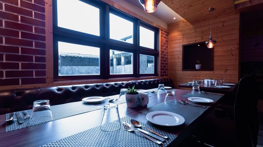 Dining setup at Sumitel Premier Inn, Siliguri, featuring neatly arranged plates, cutlery, and glasses placed beside wide windows for a bright dining experience.