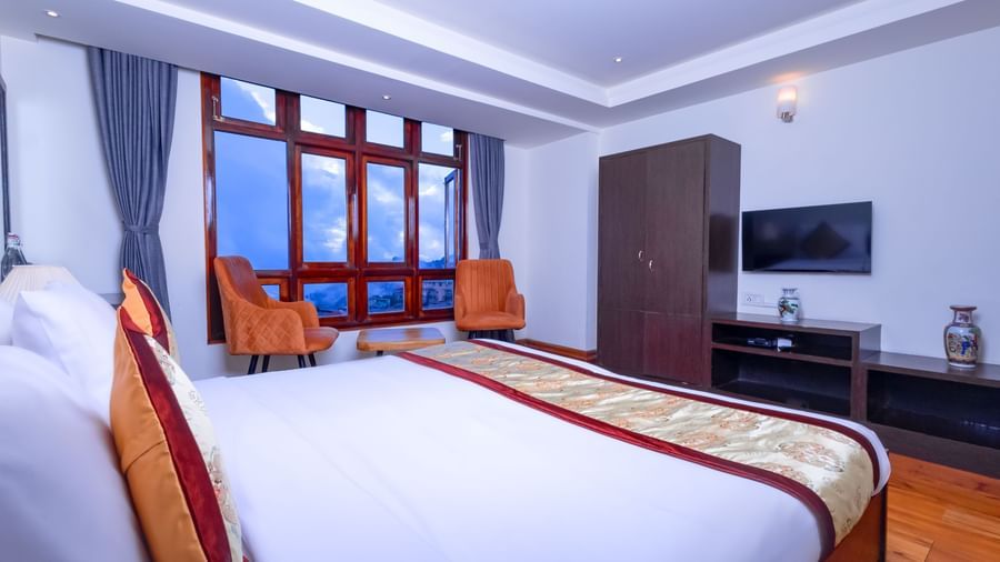 Bright guest room at Sumitel Premier Inn, Siliguri, featuring a large bed, window seating, and modern furnishings with a view through wide glass windows.