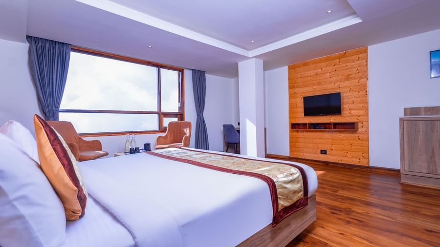 Spacious guest room at Sumitel Premier Inn, Siliguri, with a large double bed, wooden flooring, modern décor, and wide windows filling the space with natural light.