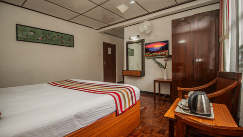 An image of bedroom featuring, a dressing table, TV, chair, table with a tea and coffee maker, and a fan - Central Hill Resort, Gangtok