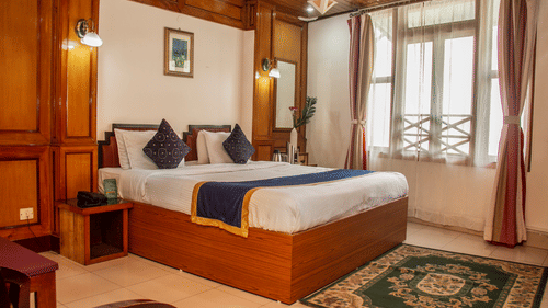 An image of a Hill Club room featuring a double size bed, a bedside table, jug, tea and coffee maker on the other table, and a mirror at Central Hill Resort, Gangtok