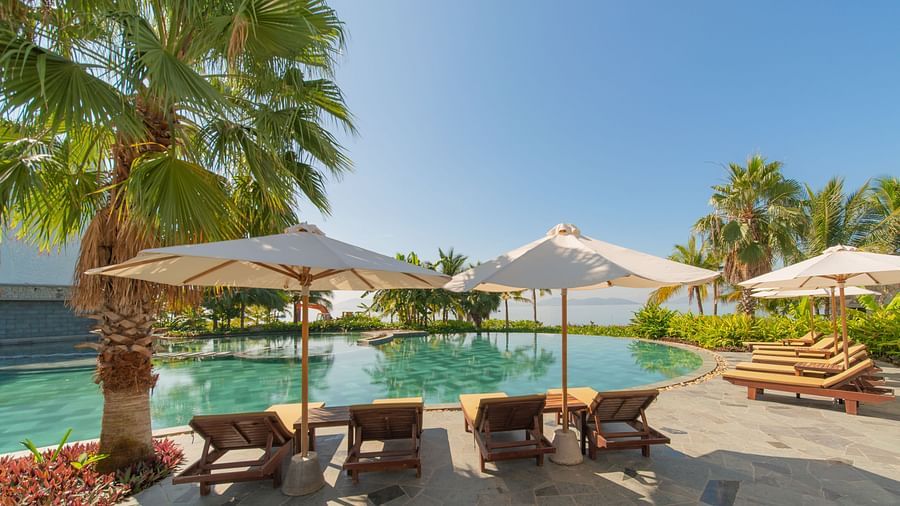 An image of a pool side with four beds placed along with overhead umbrellas for each - Alibu Resort Nha Thrang