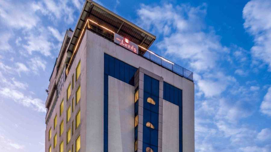 A tall and modern hotel building with its vibrant lighting illuminated at night - Lords Hotels & Resorts