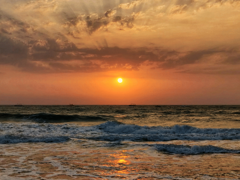A sunset at a beach with waves crashing the shore under a vibrant sky