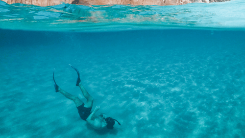 a person scuba diving as seen from above the the water with a cliff in the background