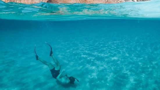 a person scuba diving as seen from above the the water with a cliff in the background