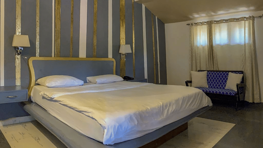 King size bed with white bedding against a blue and yellow striped accent wall, with a seating area beside it.