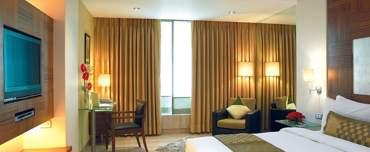 Image of a the executive room featuring a king size bed, a study table and chair, flat screen television, and an expansive window with golden curtains. | Mirage Hotel