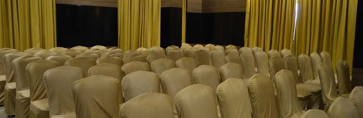 A wide-angle view of a banquet hall at The Royal Comfort, showing multiple rows of chairs ready for an event, with yellow and black curtains in the background.