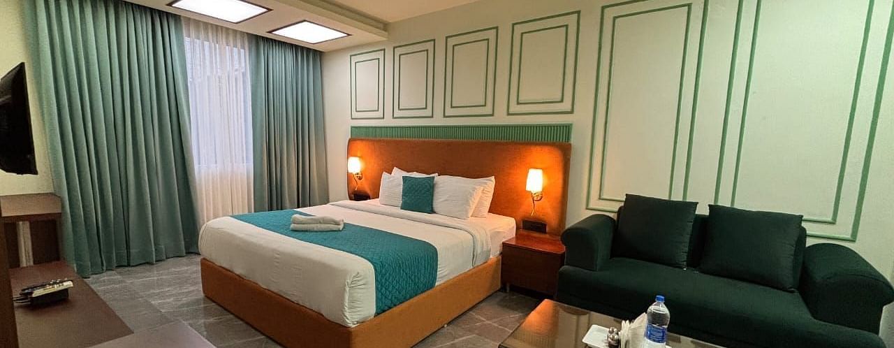 A hotel room featuring a bed, a sofa, a coffee table, and a television - Asian Suites IFFCO Chowk Metro Station, Gurgaon.