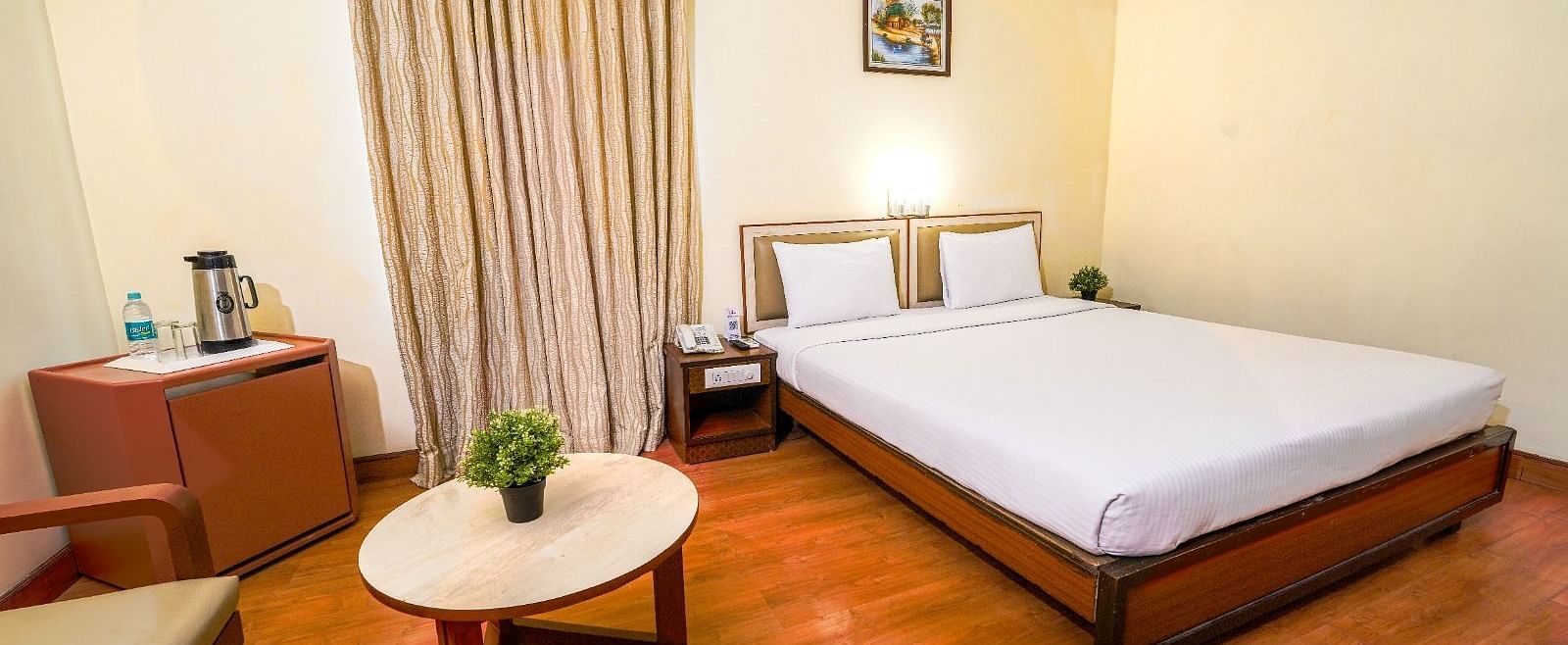 Bright hotel room with a double bed, wooden flooring, and a seating area by the window in Hyderabad near Ramoji Film City.