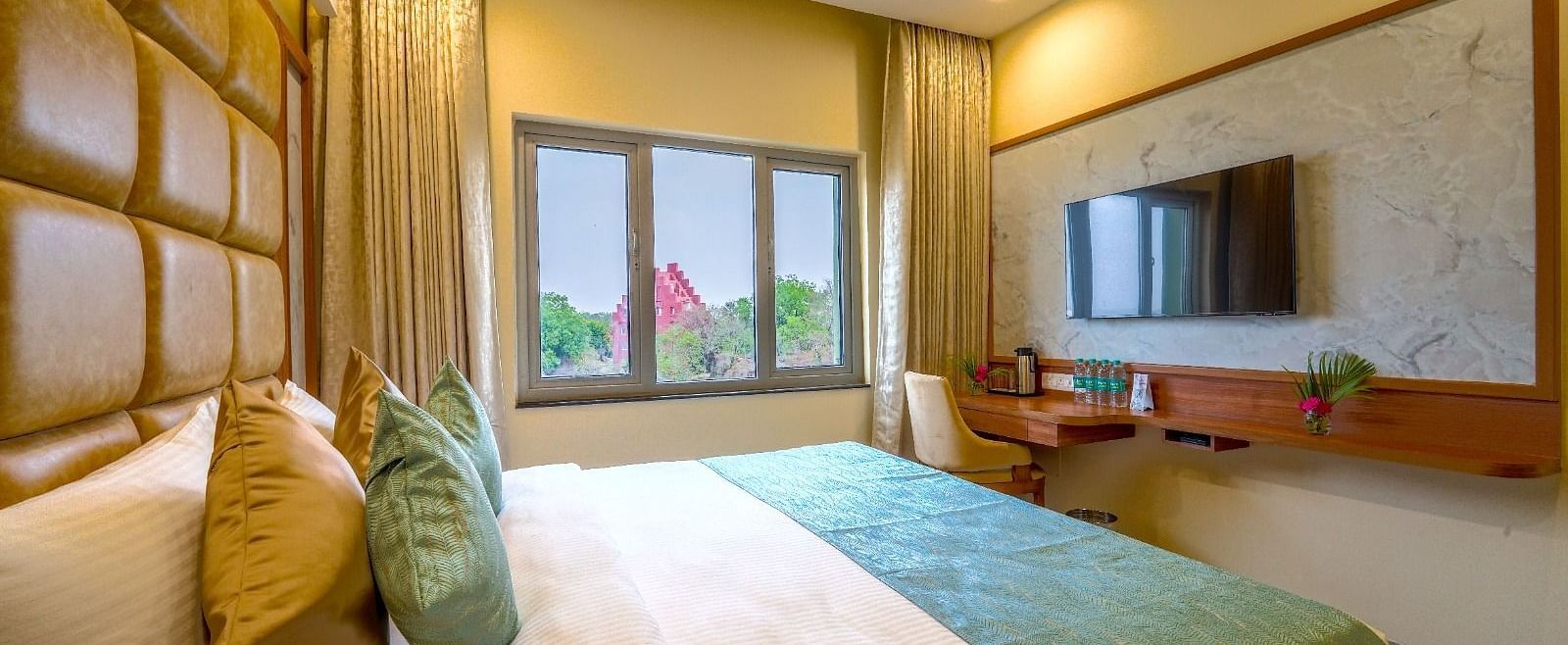 Bright and airy hotel room with a plush queen-sized bed, wooden accents, and a view of the greenery outside Tara, Comfort Hotel in Hyderabad - Ramoji Film City.