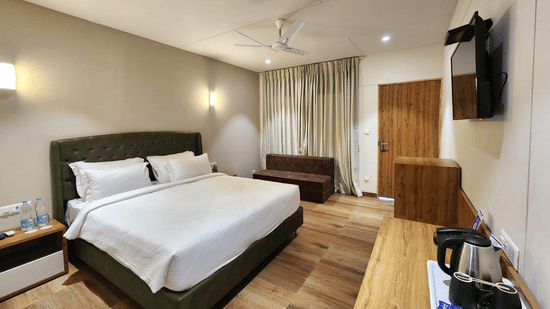 The interior view of a cottage in Daman featuring ceiling fan, a double bed, wall mounted bed lights, and a TV | VITS Daman Devka Beach