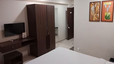 Full view shot of the Deluxe Room at Pravasa Ahmedabad featuring a wall mounted television beside a wooden wardrobe placed opposite to a double bed.