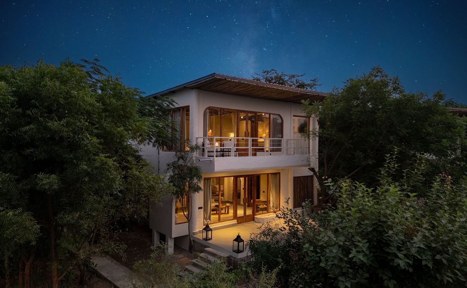 Exterior of a modern two-story villa surrounded by trees and plants.