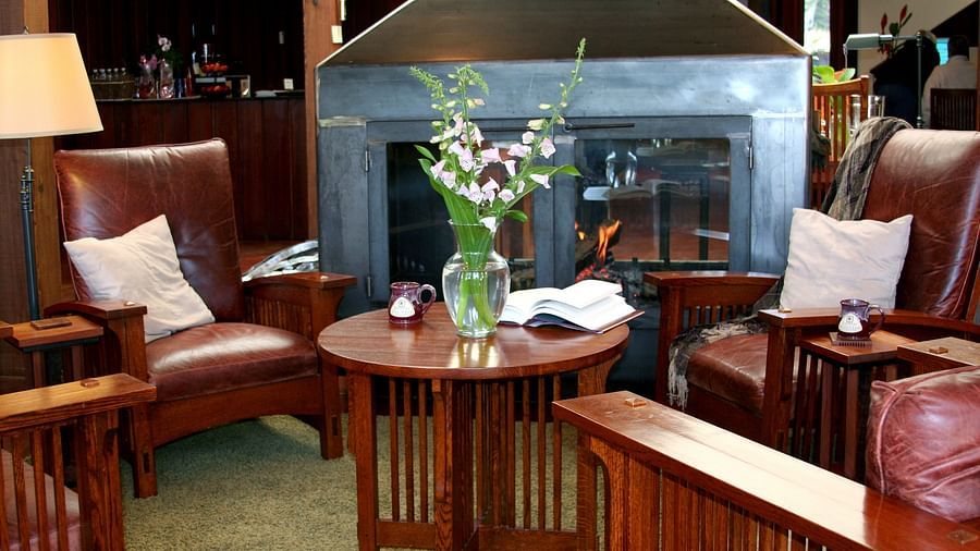 Cozy seating area with red leather chairs, a wooden table with flowers, and a fireplace in the background - Brewery Gulch Inn & Spa