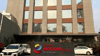 Front exterior view of the Ramada Encore by Wyndham Chandigarh Zirakpur hotel building with the main entrance and vehicles parked outside.