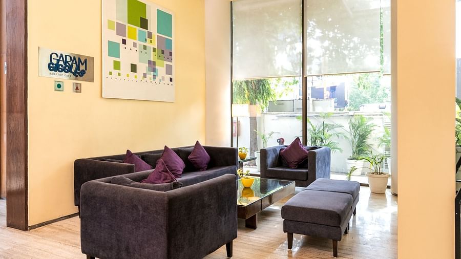  A seating area with comfy sofa and warm ambience with sign board of cafe at at Marasa Sarovar Portico, Rajkot