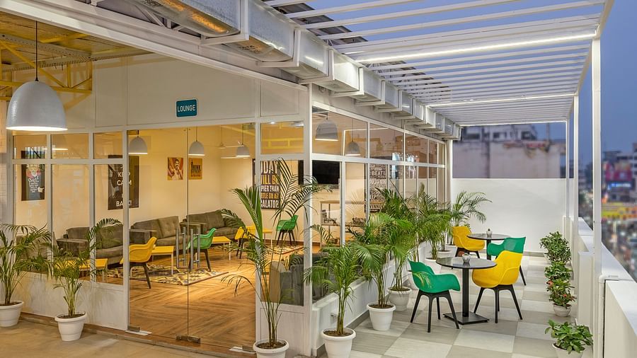 An image of a lounge featuring both indoor and outdoor seating,  with a few plants outside, beautifully lit for the evening atmosphere.