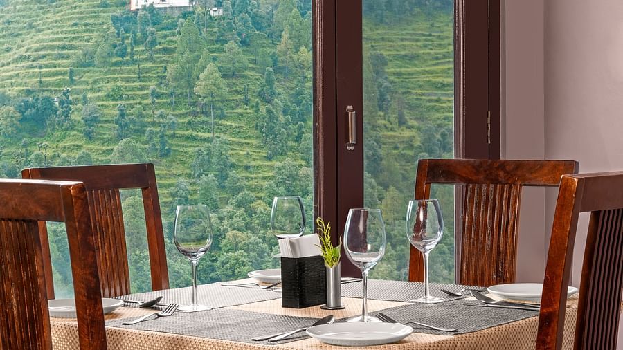 Indoor dining area with a view of terraced hills through large glass windows at BluSalzz Collection - Suvaasa Resort, Ramgarh.