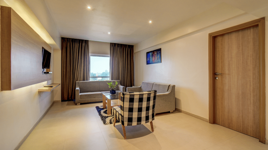 Sofas and an armchair are arranged around a low central table on a rug near a doorway. This seating area forms part of the lounge within a Suite Room at The SSK Solitaire Hotel & Banquets, Mumbai Naka - Nashik.
