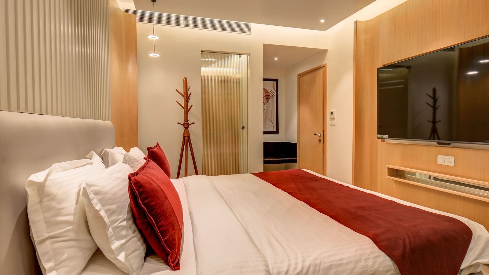 A tidy bedroom featuring a neatly made bed, a TV mounted on the wall, and a view of the door