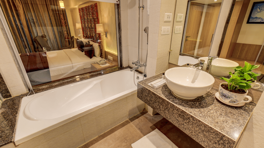 A bathtub is installed against a wall next to a stone vanity countertop featuring a ceramic wash basin. This bathroom area belongs to a Suite Room at The SSK Solitaire Hotel & Banquets, Mumbai Naka - Nashik.