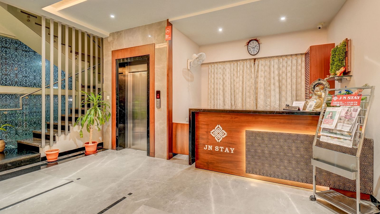 The front desk at Harigovinda's JNStay, with a lift on one side, a newspaper stand on the other, and warm lighting