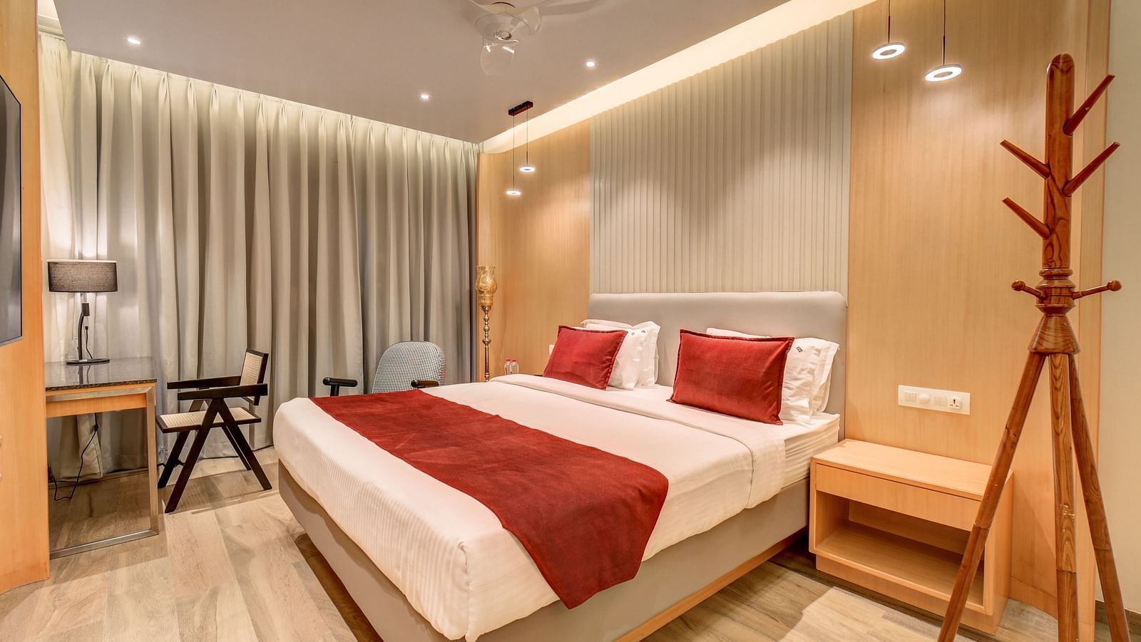 An image of a neatly arranged bed, a side table with a chair, and a coat hanger placed near to the bed