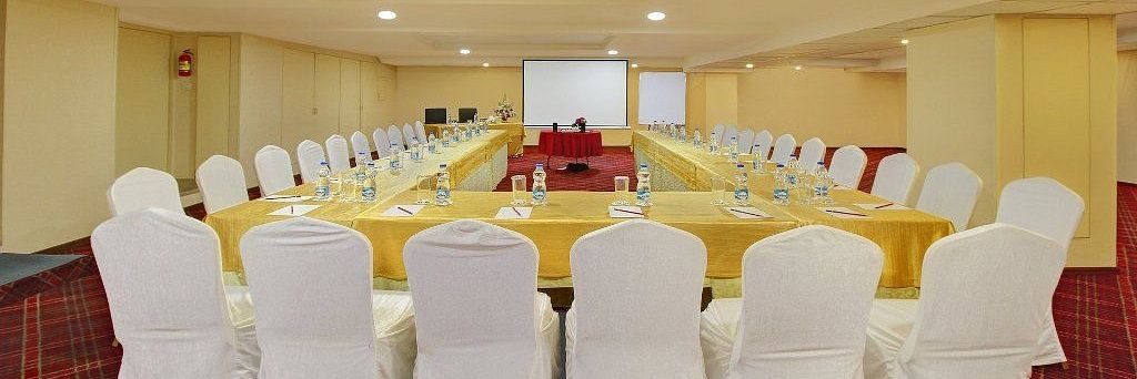 Chairs arranged around a big U shaped table for conference purposes, with limited decorations and a white screen at the front for the presenter - Monarch Hotels