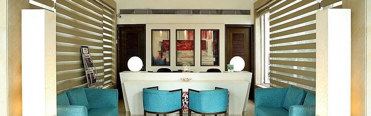 A reception area featuring stylishly arranged furniture, wall-mounted photographs, and a chandelier hanging from the ceiling at Inde Signature Tower, Gurgaon