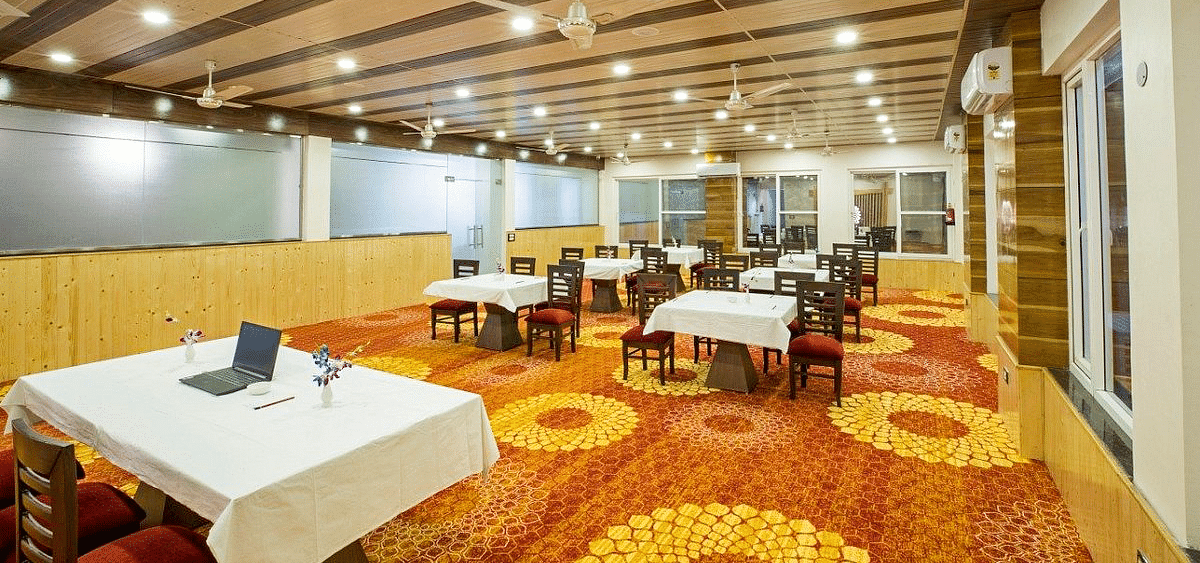 A warmly lit Banquet Hall with a fully carpeted floor along with tables set with white table cloth at Regenta Inn DLS.