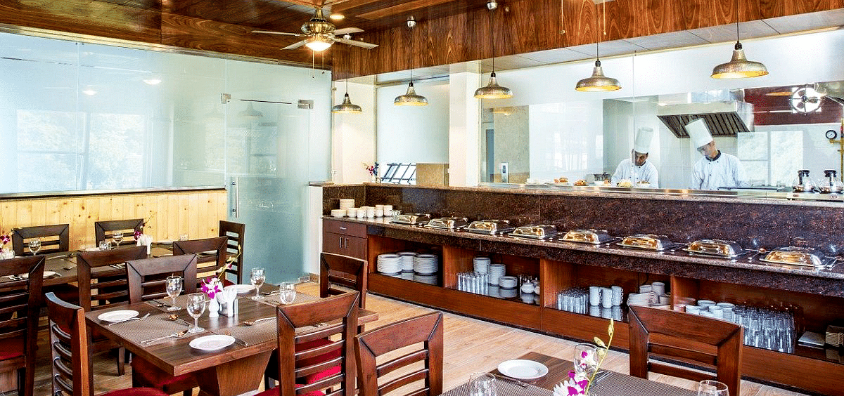 The restaurant at Regenta Inn DLS featuring the kitchen separated by a glass partition with a buffet counter in front of it.
