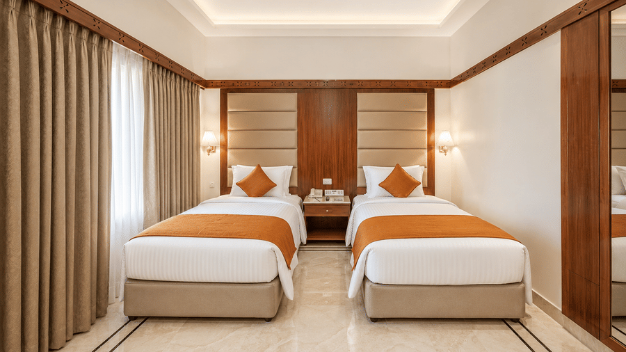 A room with twin beds, spreads, pillows, and curtains at raj park, Chennai.