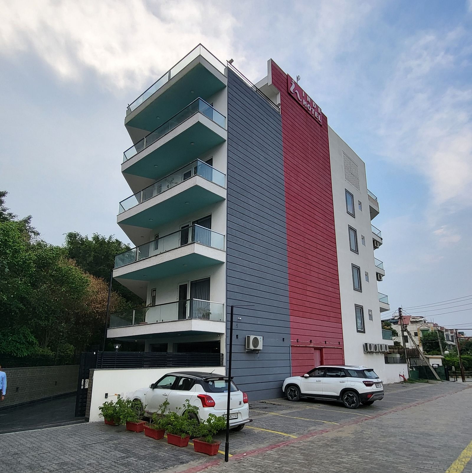 A facade of Inde Hotel Golf Course Extension featuring multiple storeys and balconies on each floor, and cars parked on the lawn