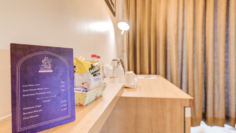 A menu card stands on a long wooden counter next to a basket of refreshments. This interior view highlights the amenities inside a Suite Room at The SSK Solitaire Hotel & Banquets, Mumbai Naka - Nashik.