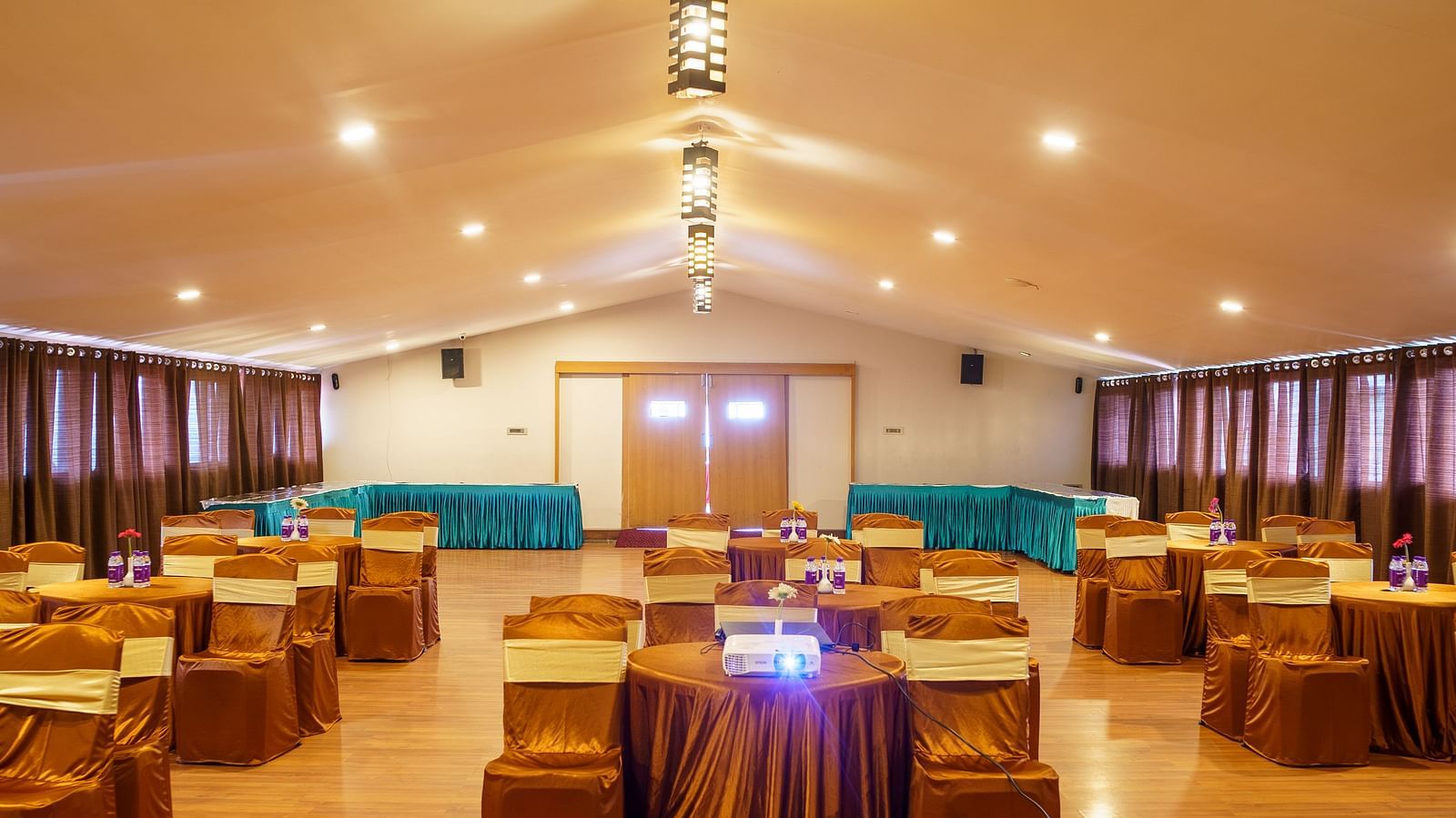 A brightly lit conference room at Orsino Hotel and Spa is set up with round tables covered in gold cloths and chairs draped in gold fabric.