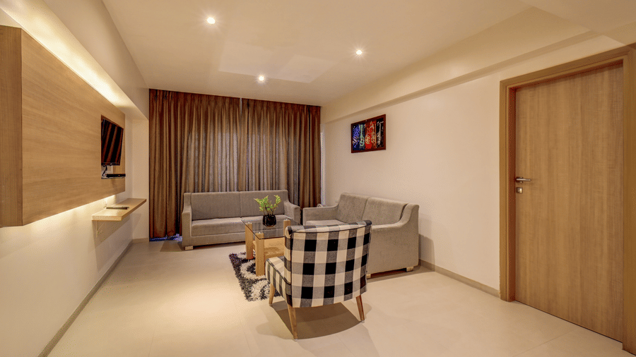 A seating arrangement with sofas and a patterned armchair sits configured near a curtained window. This lounge space is situated inside a Suite Room at The SSK Solitaire Hotel & Banquets, Mumbai Naka - Nashik.