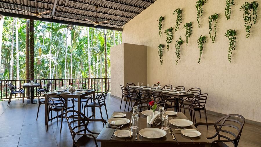 Our multi-cuisine restaurant with wooden tables and chairs and a wall with plants mounted on it - Stone Wood Nature Resort, Gokarna