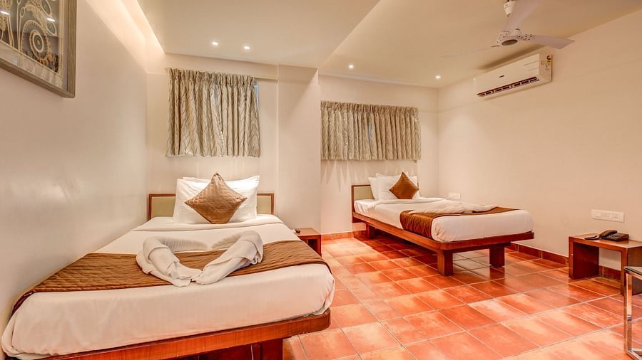 A spacious room at Harigovinda's JNStay with two beds, windows covered by curtains, and a wall-mounted AC